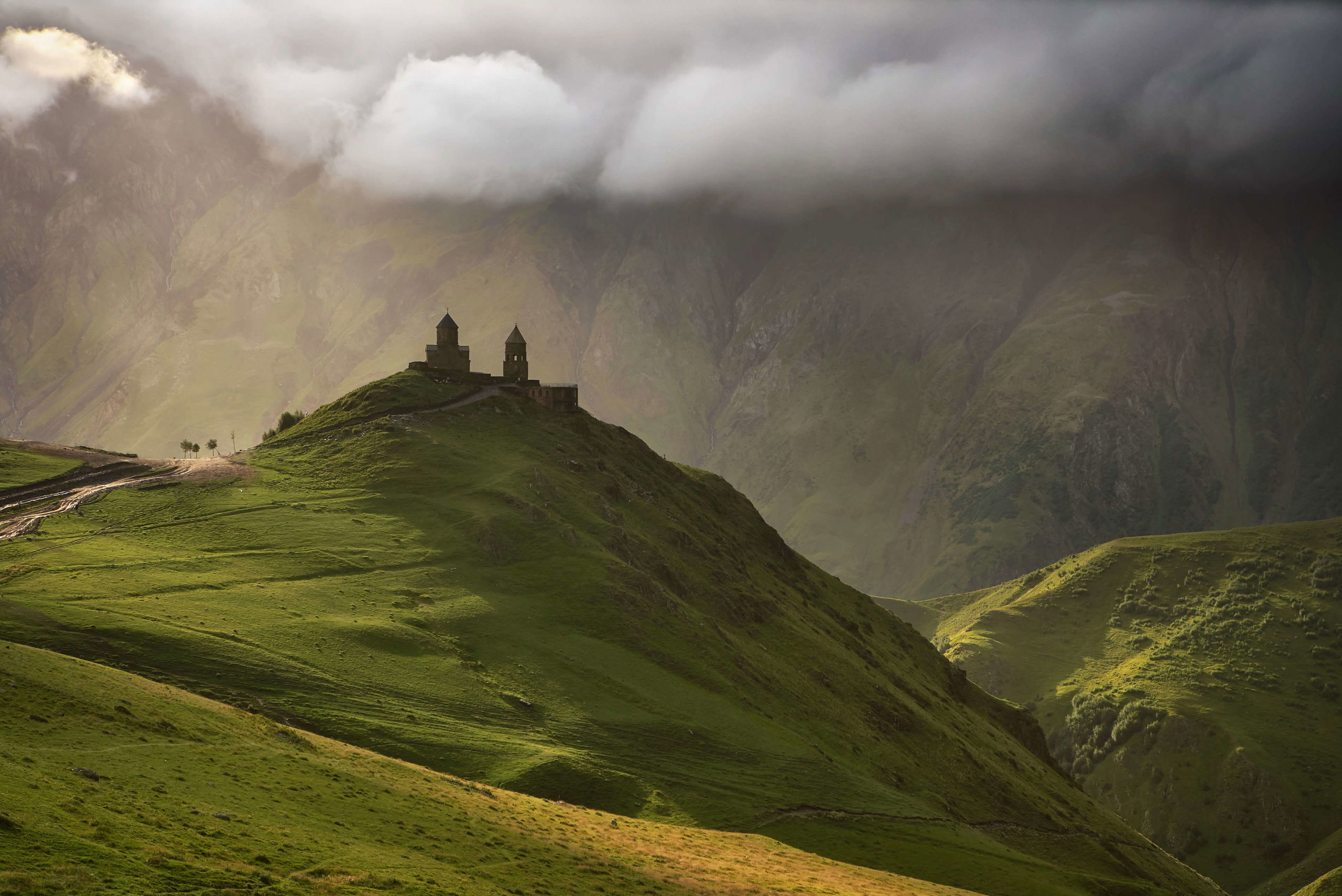 The iconic Gergeti Trinity Church in the Caucasus Mountains, enveloped in mist with dramatic lighting.