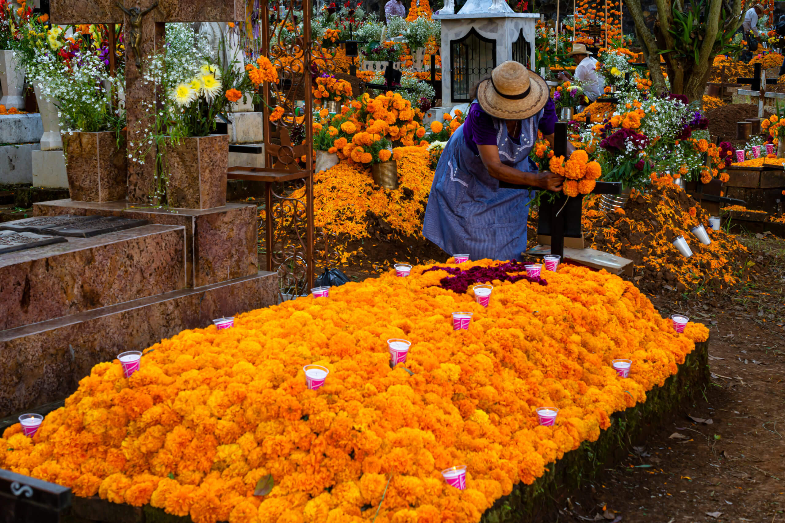 Oaxaca 2020_A person decorates a grave with bright orange marigolds and candles during Día de los Muertos in Oaxaca, Mexico, honoring loved ones with vibrant floral offerings.
