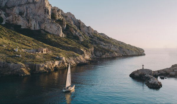 Sailboat navigating turquoise cove beneath limestone cliffs in the Calanque