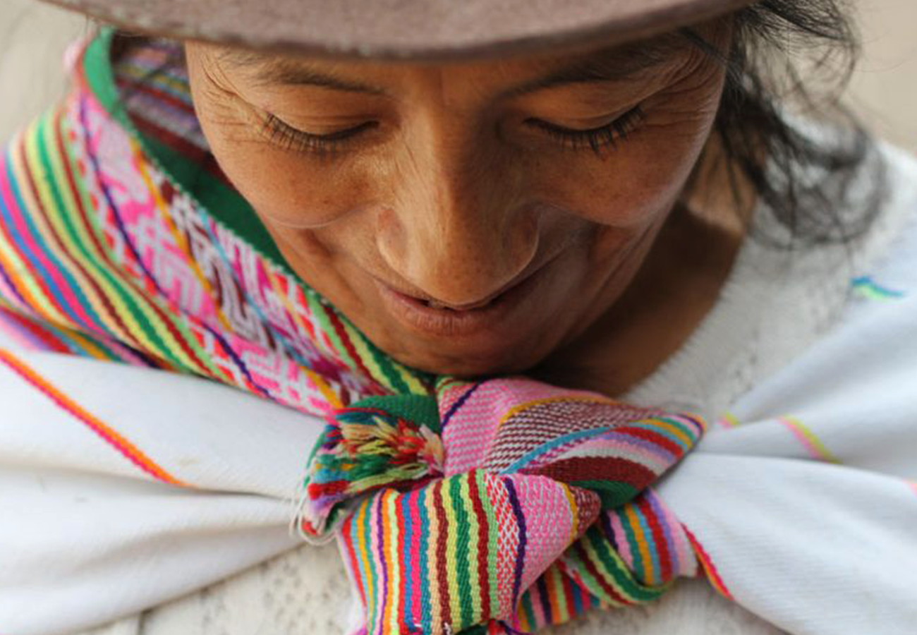 A close-up of a local Andean woman wearing a colorful, handwoven shawl, smiling gently.