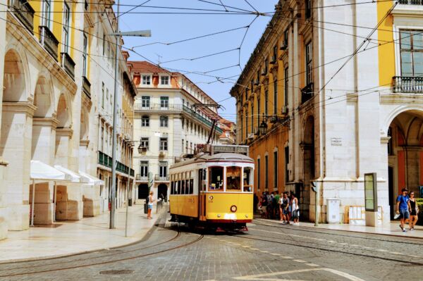 Portugal 2023_ iconic yellow tram passing through historic streets in Lisbon, Portugal, surrounded by elegant architecture and vibrant city life on a sunny day