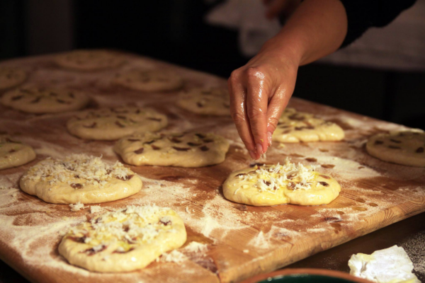 Close-up of a chef’s hand sprinkling toppings onto freshly prepared flatbread dough on a floured wooden surface. This image captures the hands-on culinary immersion and farm-to-table experiences offered in regions like Puglia or Sicily with Modern Adventure.