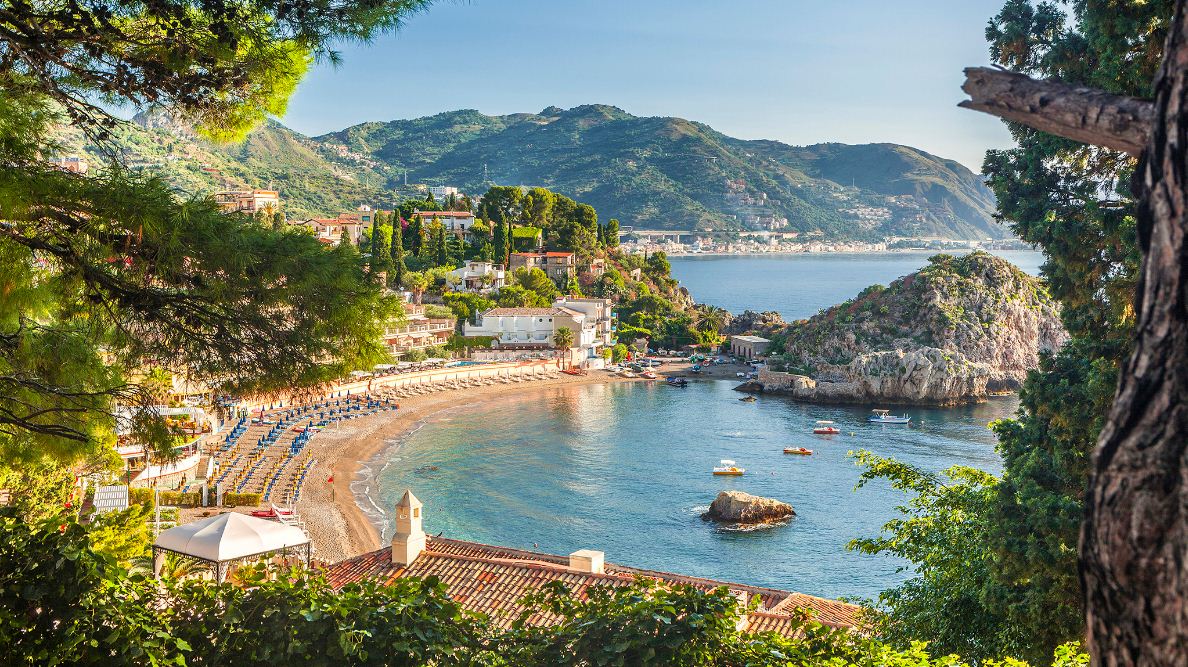 Crystal-clear waters and curved coastline of Taormina, Sicily, surrounded by green hills and Mediterranean villas.