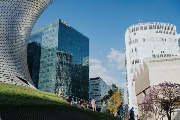 A sunlit view of contemporary urban architecture in Mexico City, featuring the striking hexagonal-tiled exterior of the Museo Soumaya alongside sleek glass skyscrapers. This scene in the vibrant Polanco neighborhood captures the fusion of art, culture, and modern design that defines a luxury Mexico city tour.