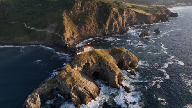 An aerial view of the stone bridge and winding stairs leading to the hermitage of Gaztelugatxe. This iconic islet near Bermeo is a crown jewel of the Basque Country coastline, known for its dramatic cliffs and cinematic scenery.