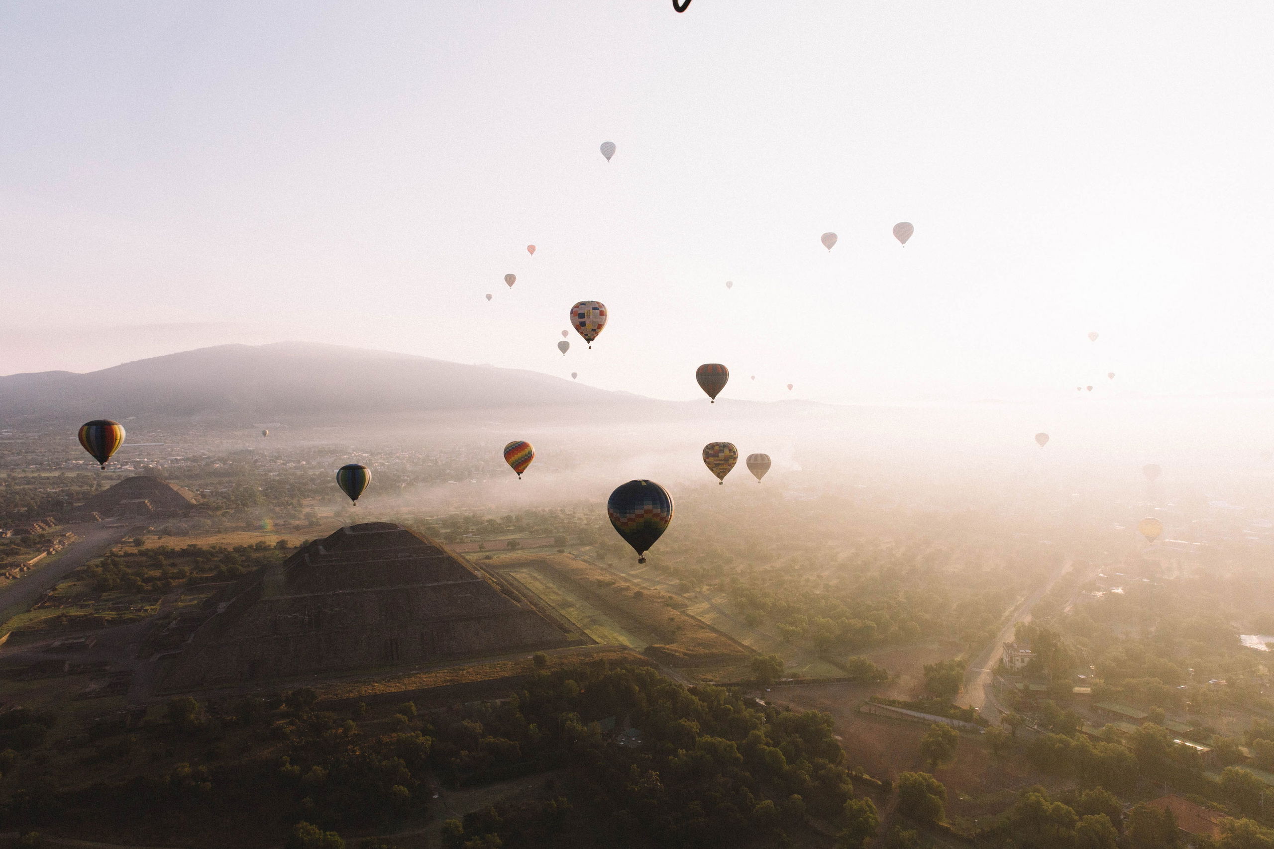Colorful hot air balloons rise over the ancient pyramids of Teotihuacan at sunrise, offering breathtaking views of Mexico’s historic landscape.