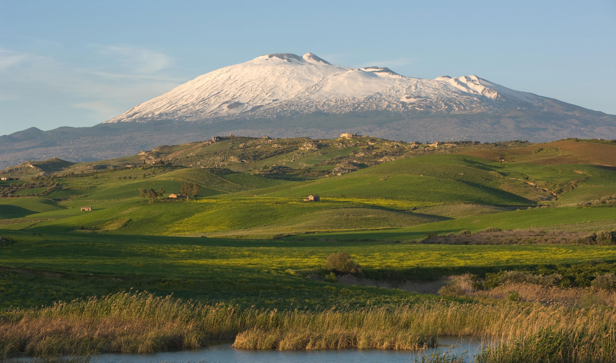 Snow-capped Mount Etna volcano rising above green Sicilian countryside and wetlands