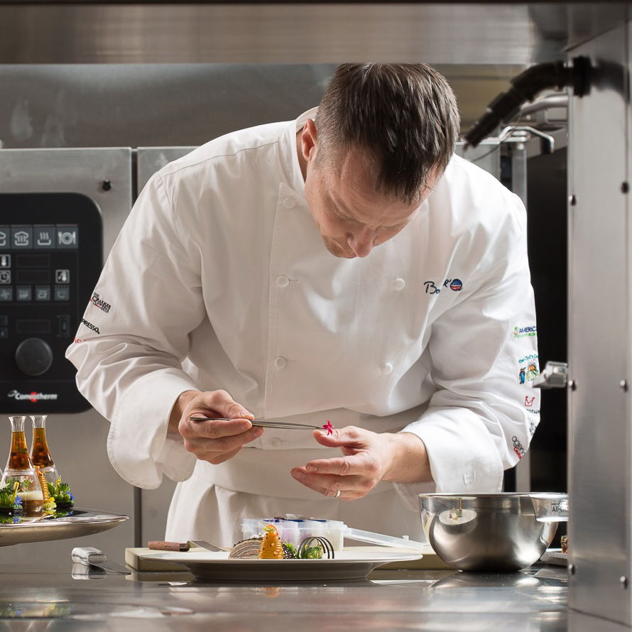 Chef Philip Tessier carefully plating a dish in a professional kitchen
