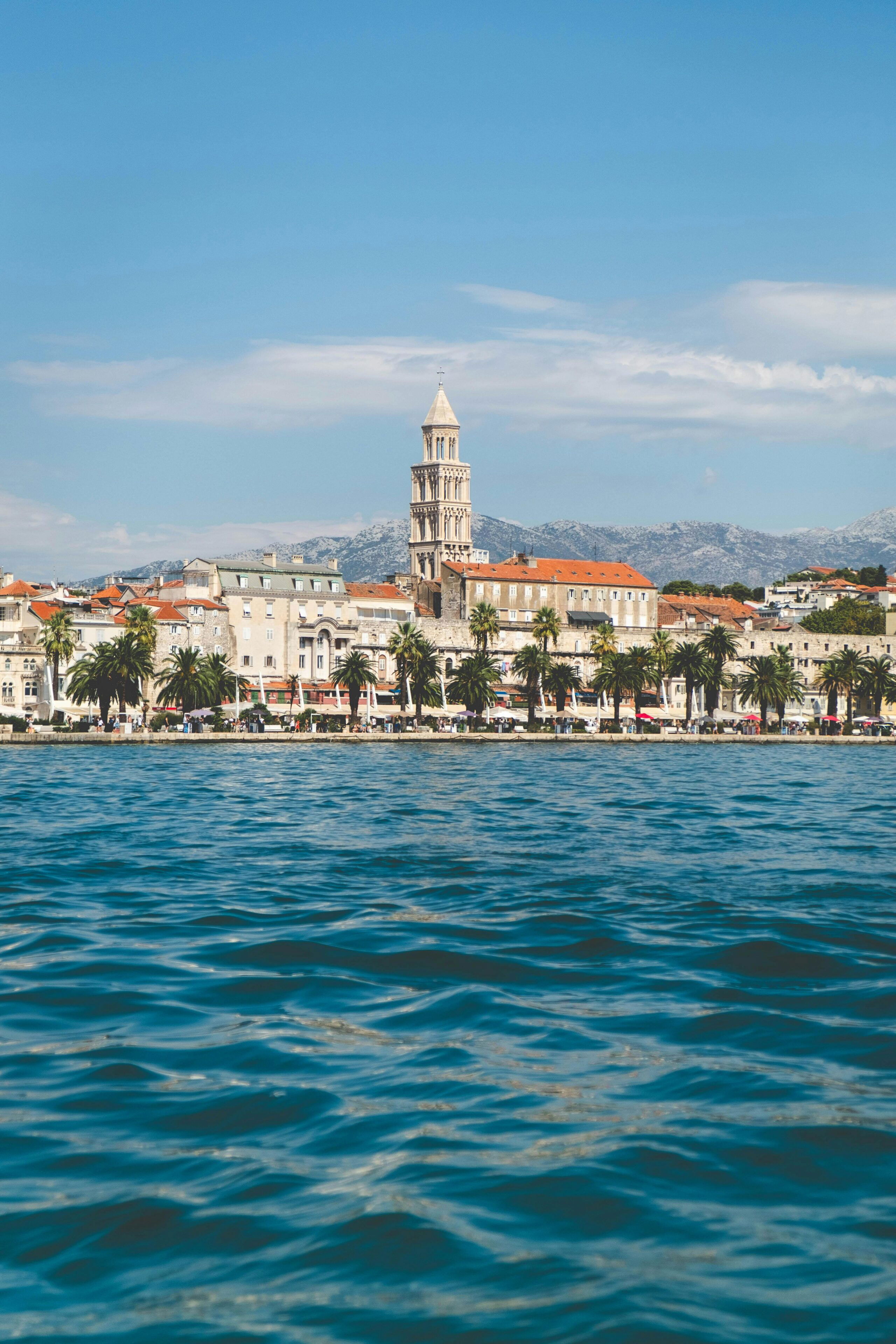 Seaside view of Split, Croatia, with the bell tower of Diocletian’s Palace rising above red rooftops and palm-lined waterfront.