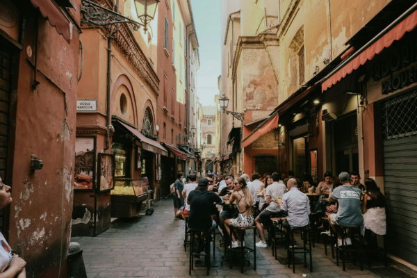 Emilia-Romagna 2025_People enjoying food and drinks at outdoor tables along a lively narrow street in Bologna’s historic center.