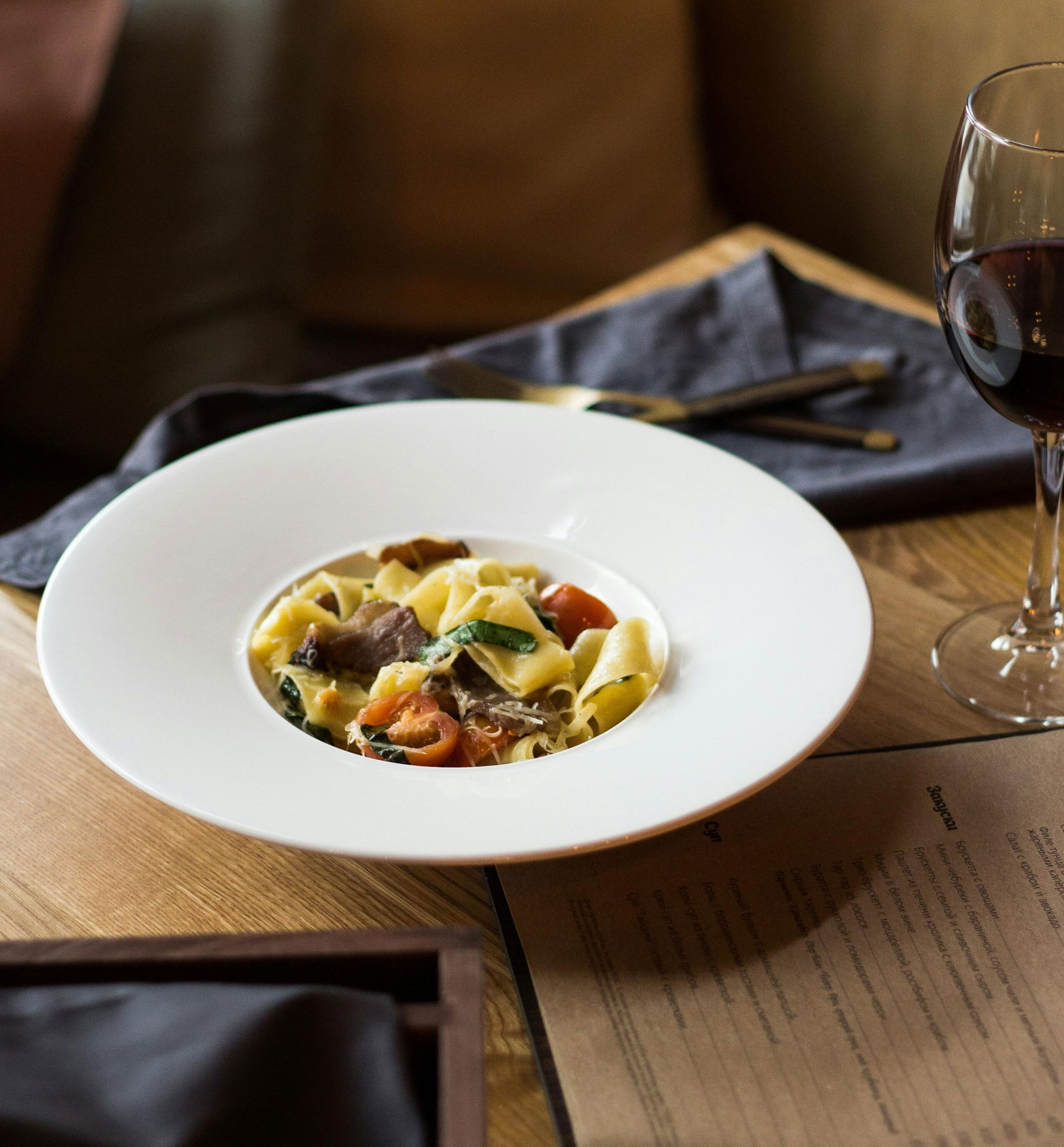 Emilia-Romagna 2025_Homemade pappardelle pasta with meat ragu and a glass of red wine served in a cozy Bologna restaurant.