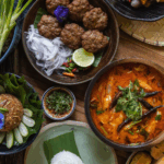 Thailand 2026_ A colorful spread of traditional Thai cuisine, including spicy red curry, fried rice, fresh vegetables, meat patties, and dipping sauces, beautifully arranged on a wooden table with banana leaves and edible flowers.