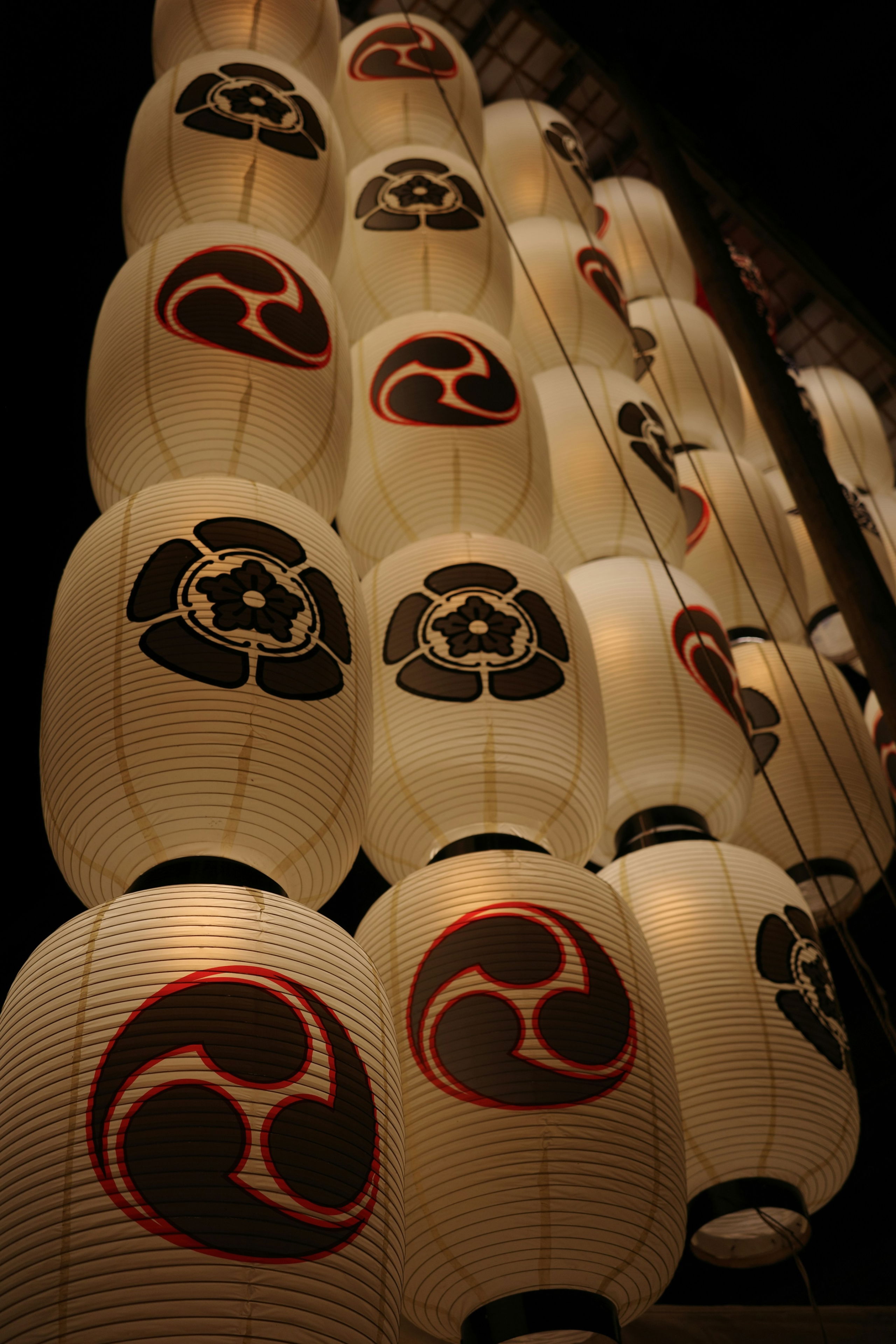 Traditional Japanese lanterns bearing family crests hang in neat rows during Kyoto’s Gion Matsuri festival, softly glowing against the night sky.