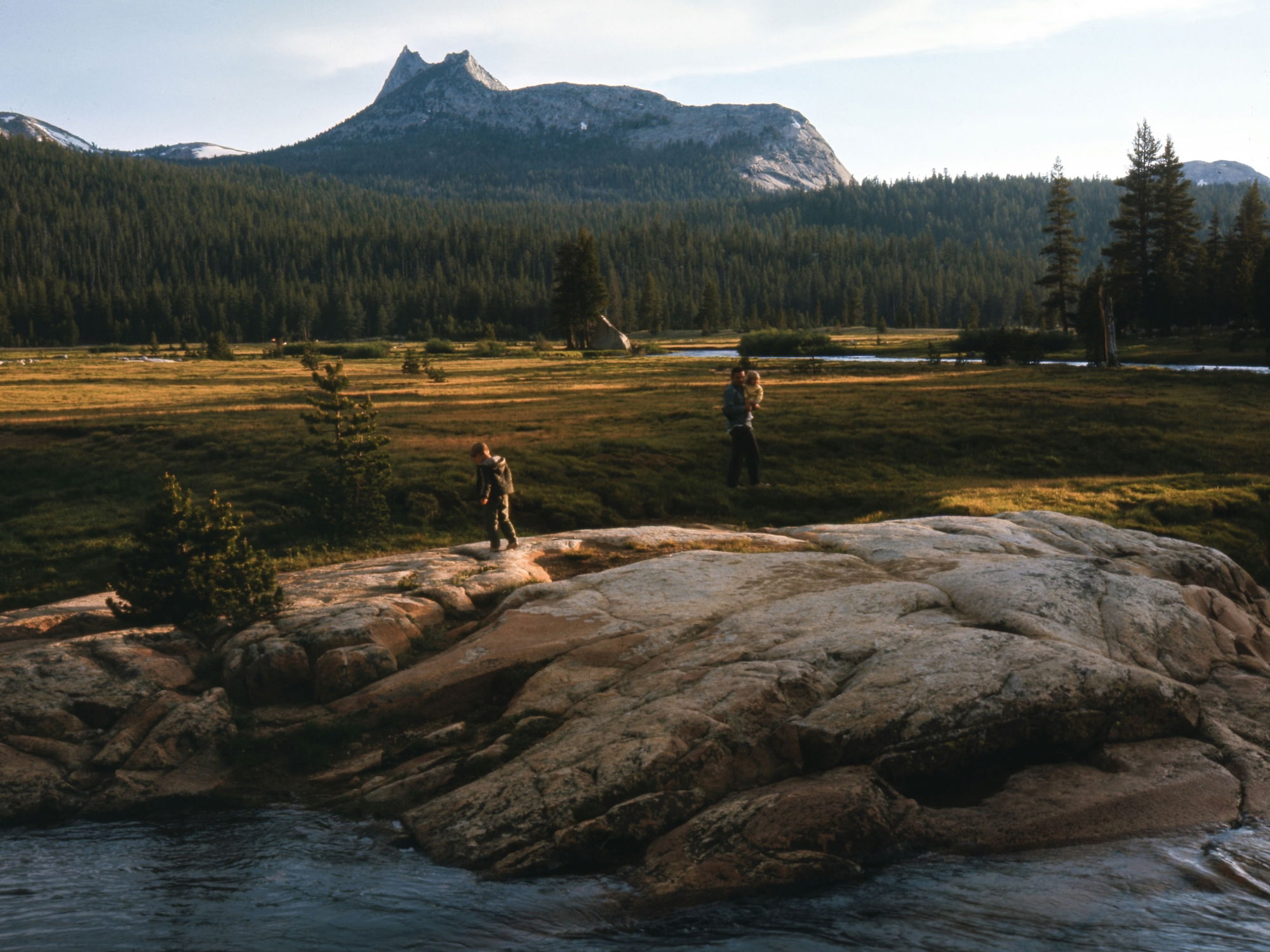 Family walking on granite rocks by a river with Cathedral Peak in the background, Yosemite National Park